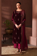 Woman in a maroon traditional outfit with intricate patterns standing in a warm-toned room.
