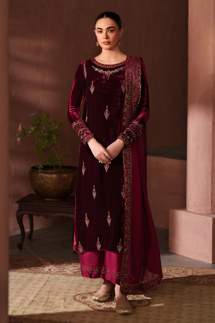 Woman in a maroon traditional outfit with intricate patterns standing in a warm-toned room.
