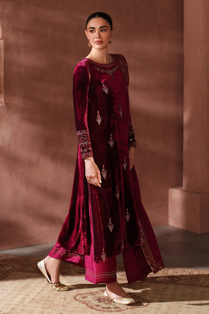 Woman wearing a burgundy embroidered traditional outfit against a warm-toned wall.