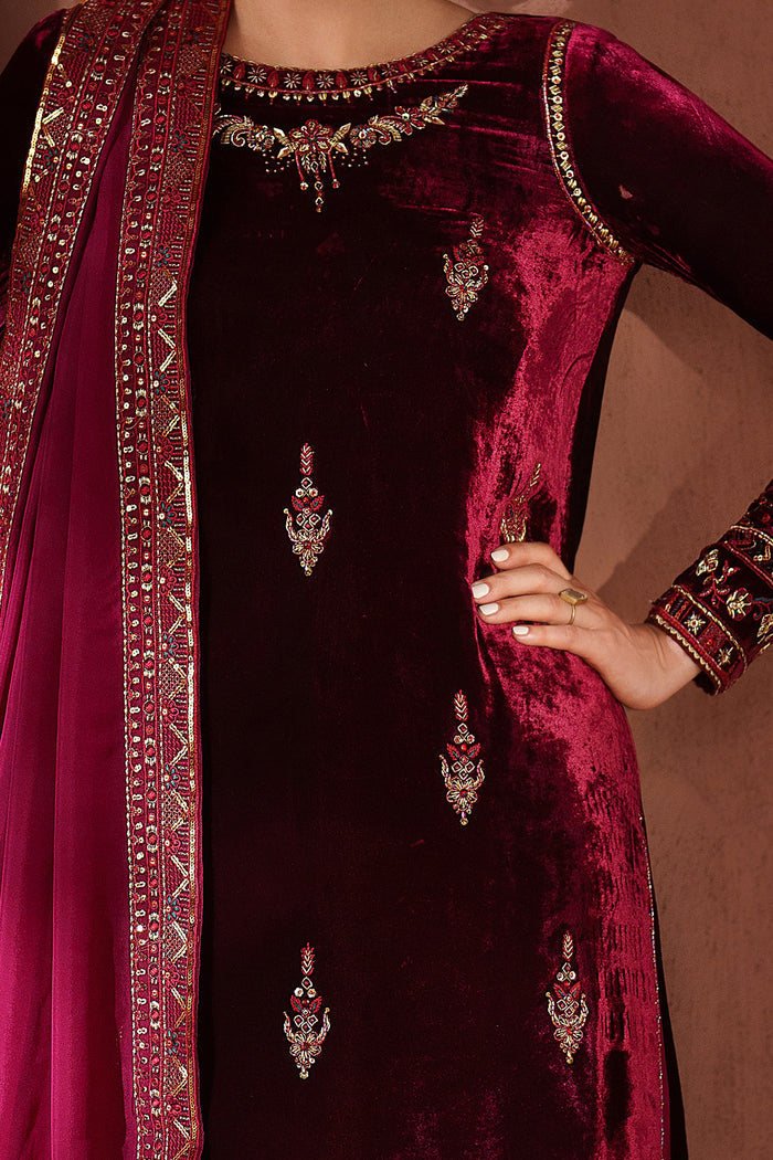 Maroon velvet outfit with intricate embroidery and jewelry on a brown background