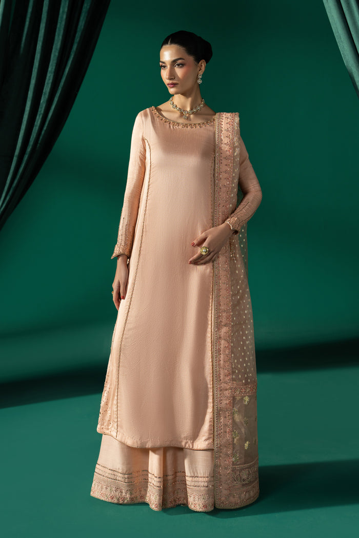 Full-length front view of Azba showing the peach Indian Raw Silk frock, boat neckline and wide PK Raw Silk sharara.