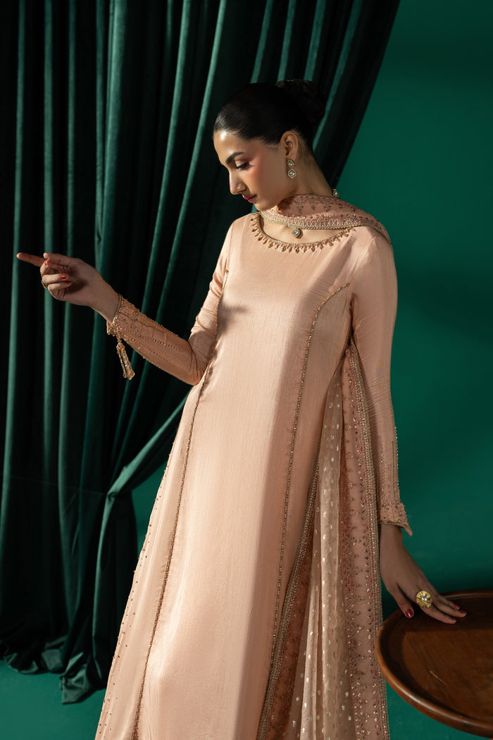 Three-quarter view of Azba highlighting the extended sleeve, embroidered frock panels, side slit and flowing peach silhouette.