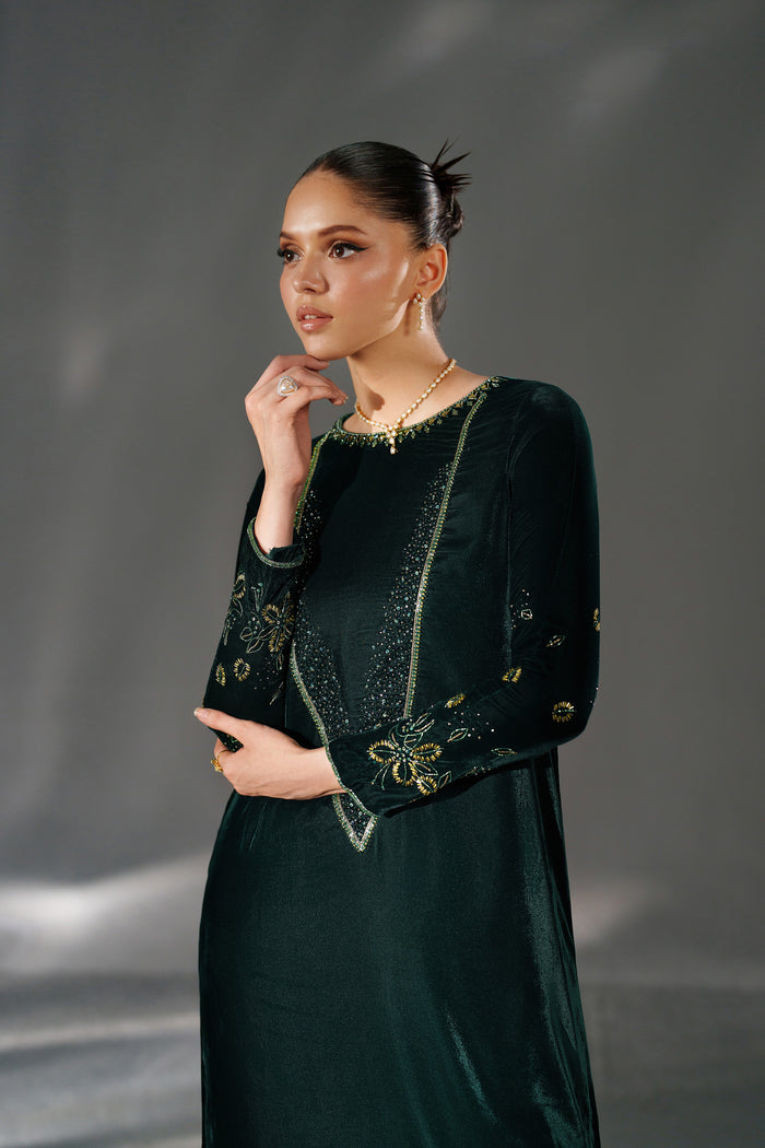 Woman wearing a dark green dress with gold embellishments against a gray background