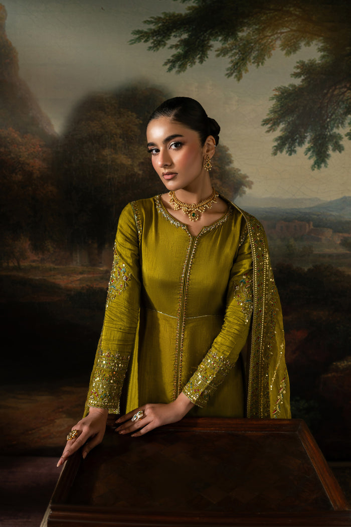 Seated view of Ghina highlighting the olive green embroidered frock, open slit detail and coordinated dupatta styling.