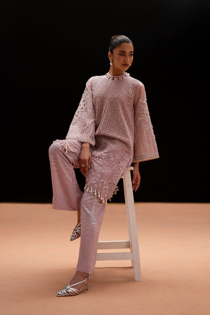 Seated view of Gigil highlighting the geometric embroidery, relaxed shirt silhouette and embroidered bell-bottom trousers.