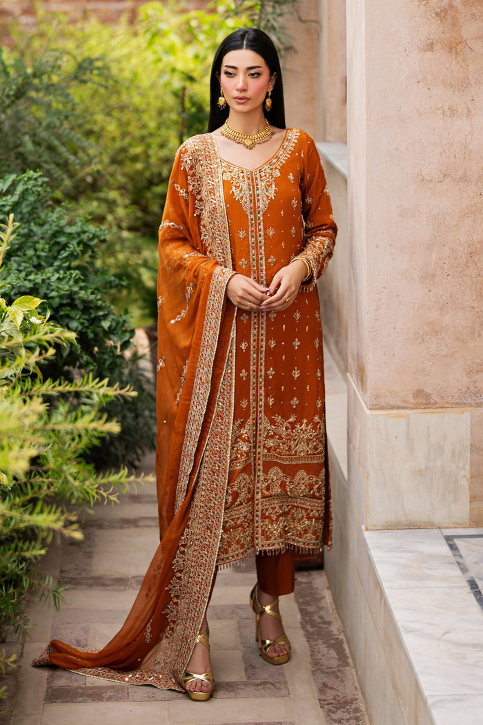 Rust Indian raw silk formal gown by NAQSHI with full embroidery, rounded neckline, long sleeves, wide embroidered hem, paired with matching trousers and chiffon dupatta.