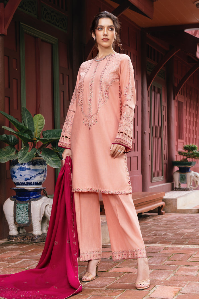 Woman in a peach embroidered outfit standing in front of a traditional building.