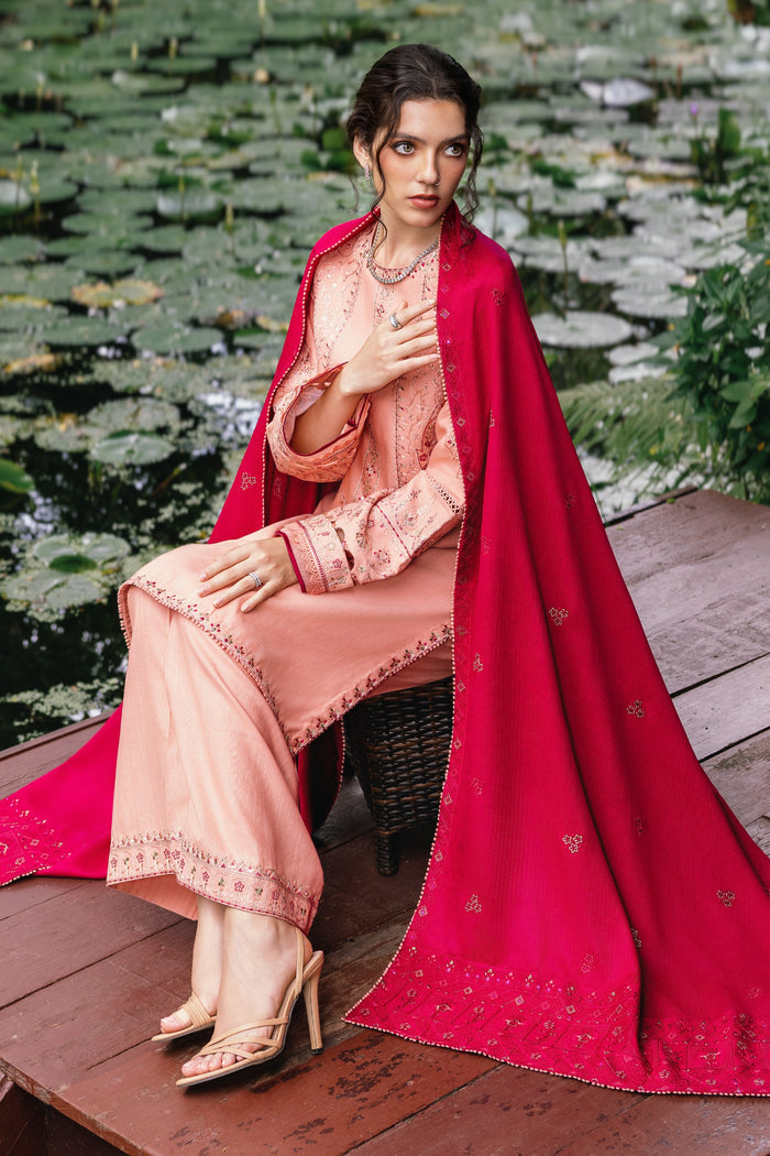Woman in a peach outfit with a red dupatta sitting on a wooden platform with water lilies in the background.