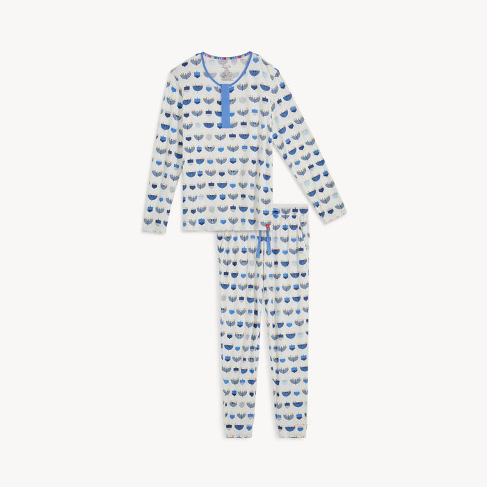 A two-piece men's pajama set in white fabric featuring a long-sleeve top with hidden magnets and matching joggers, both detailed with an all-over print of blue and silver dreidels and menorahs, by Magnetic Me.