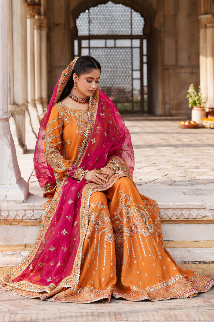 Sitting pose of NAQSHI Mahzaeeb orange event dress with sharara trousers and pink embroidered dupatta for formal celebrations.