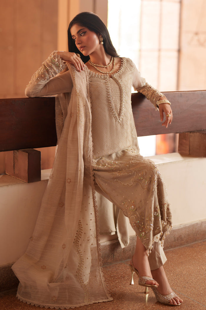 Seated styling shot of NAQSHI Minera dusty beige formal outfit with embroidered khadi net shirt, raw silk trousers and cotton organza dupatta