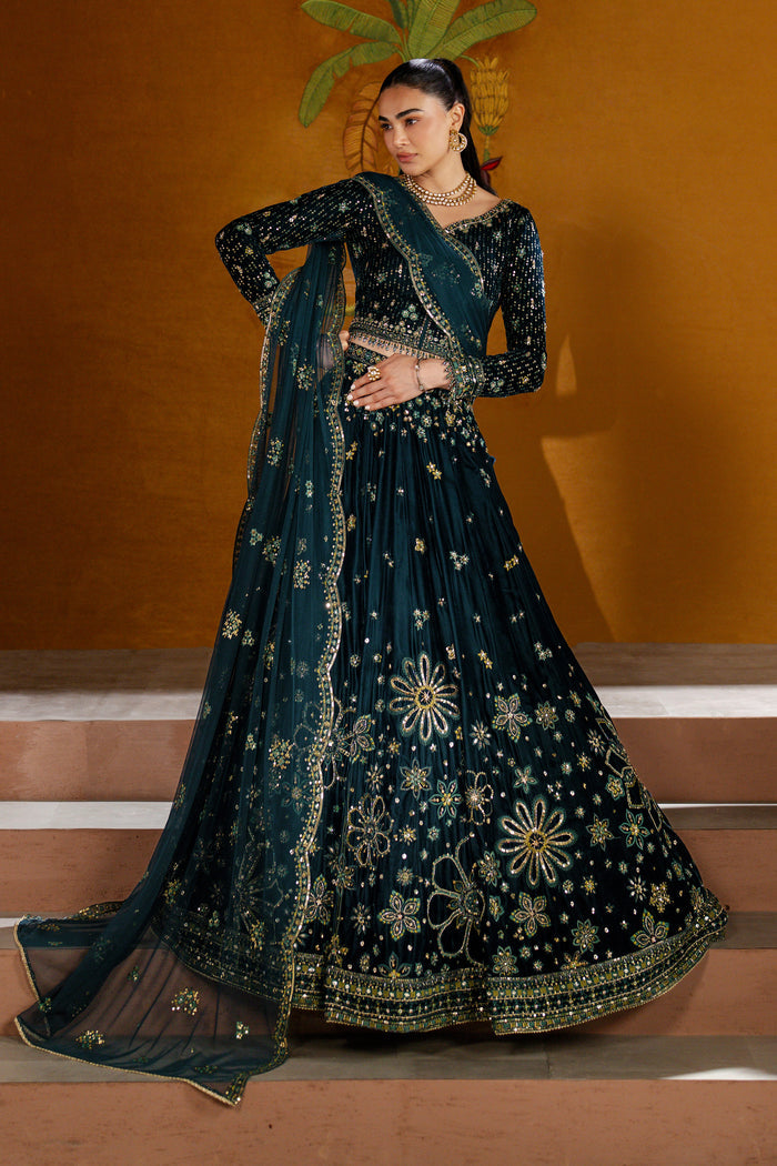 Woman in a dark blue embroidered traditional outfit with a matching dupatta against an orange wall.