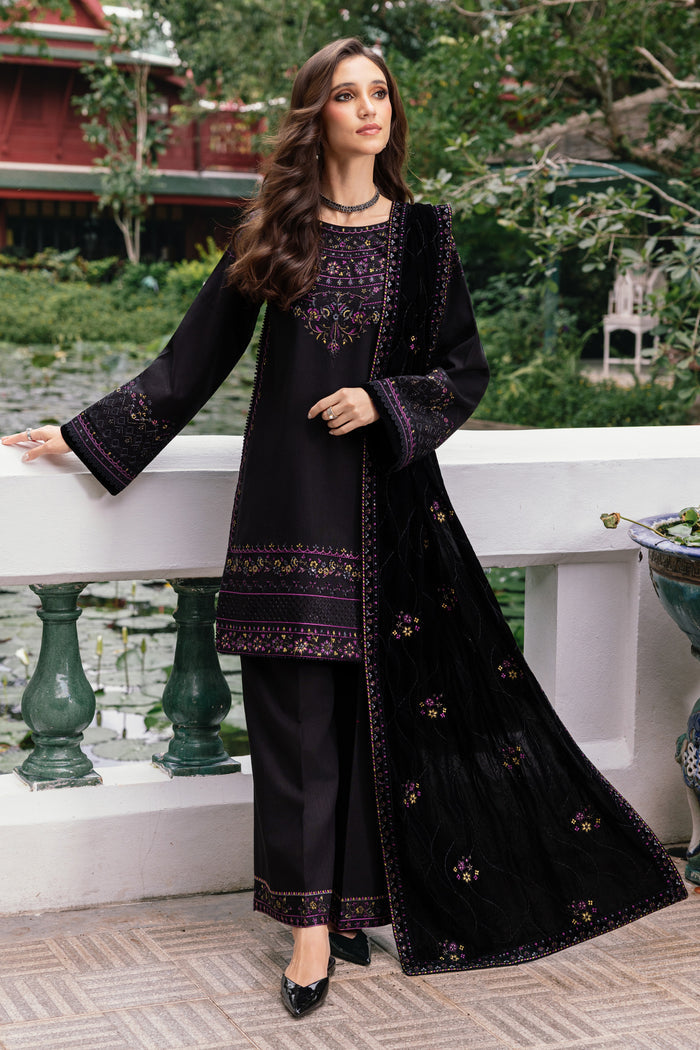 Woman in a black embroidered outfit standing outdoors with greenery in the background