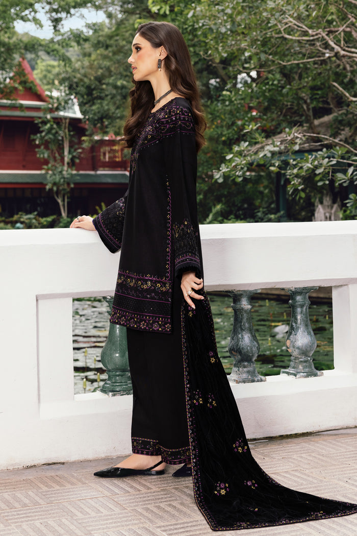 Woman in a black embroidered outfit standing on a bridge with greenery in the background