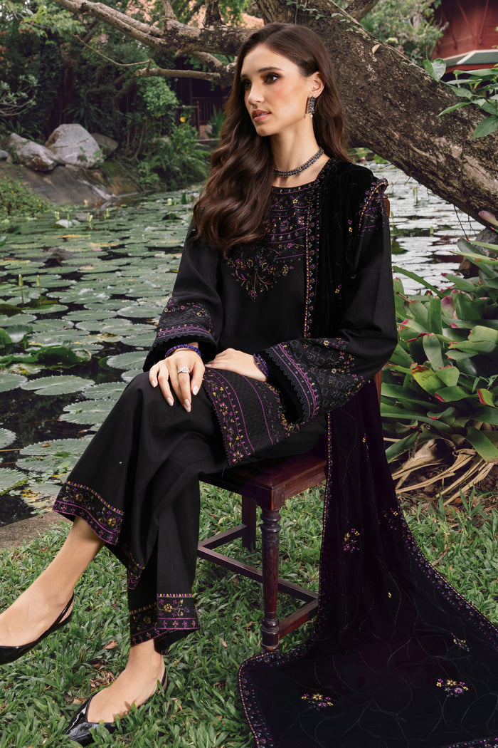 Woman in black embroidered outfit sitting by a pond with lily pads.