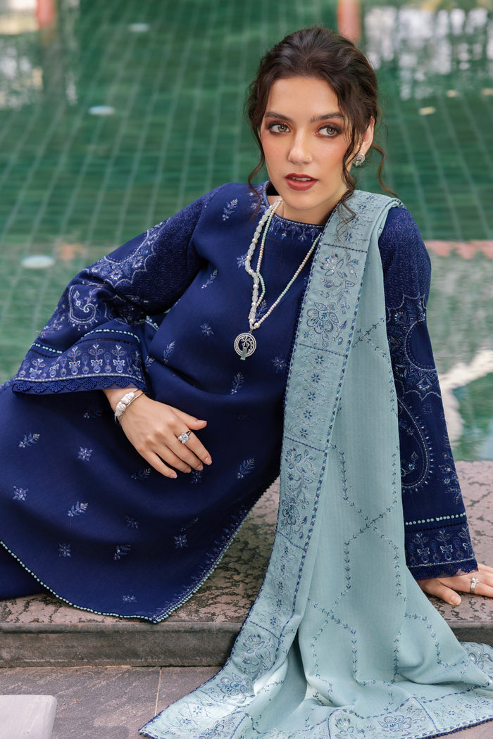 Woman in traditional blue and green outfit with jewelry, sitting on a stone bench.