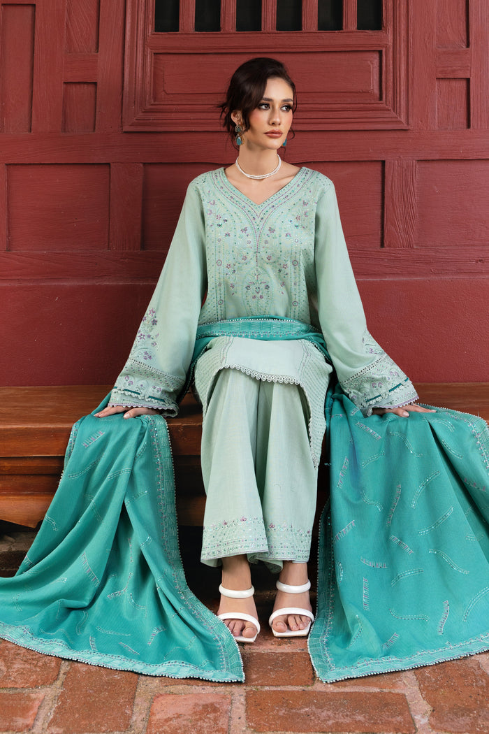 Woman in a teal traditional outfit sitting on a bench with a red wall background