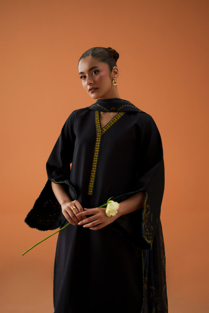 Model wearing Vera black embroidered lawn shirt with contrast V neckline, printed chiffon dupatta, and cambric shalwar for semi-formal Eastern wear.