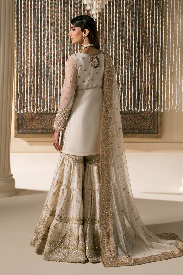 Back side pose of Zaleena honey beige Nikkah outfit showing smooth fall of organza shirt and wide layered gharara flare with net dupatta, modest ready made bridal formal wear.