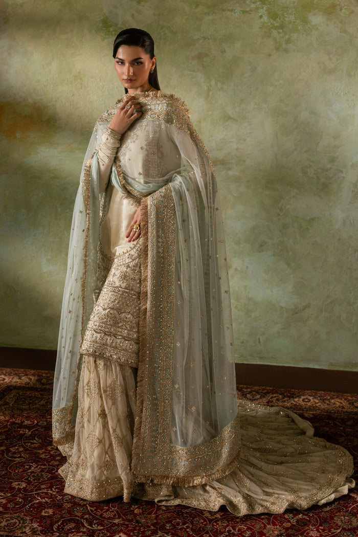 Side drape view of Zemira beige peach bridal dress with flowing farshi gharara and light net dupatta spread, graceful ready made Nikkah outfit.
